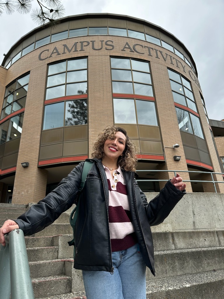 Dora at the Thompson Rivers University Campus Activity Center, smiling on the outdoor steps in front of the building